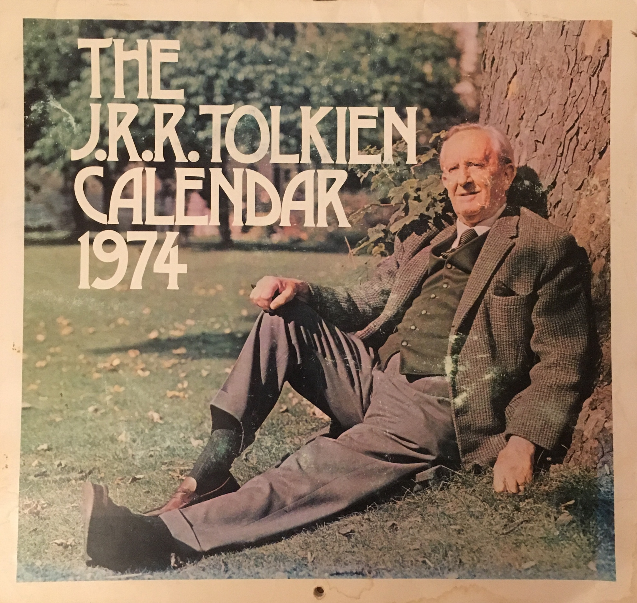 JRR Tolkien sitting against a tree with a park in the background.