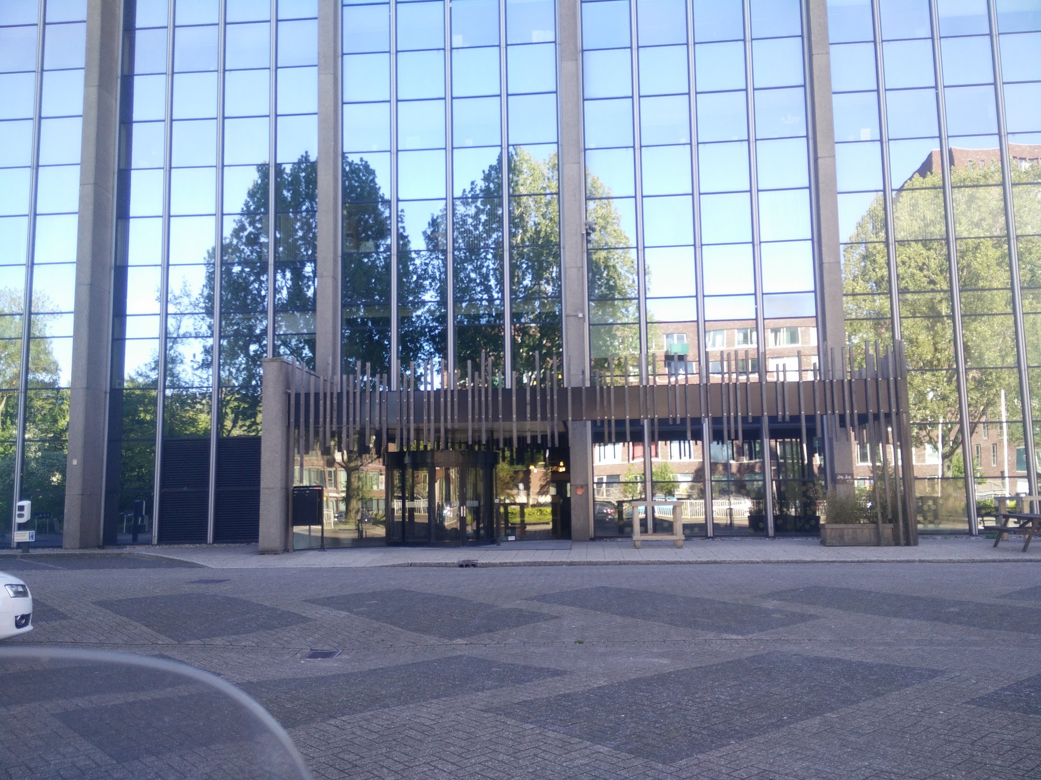 The modern front lot and facade of the building, covered minly in glass panels and no plants in front