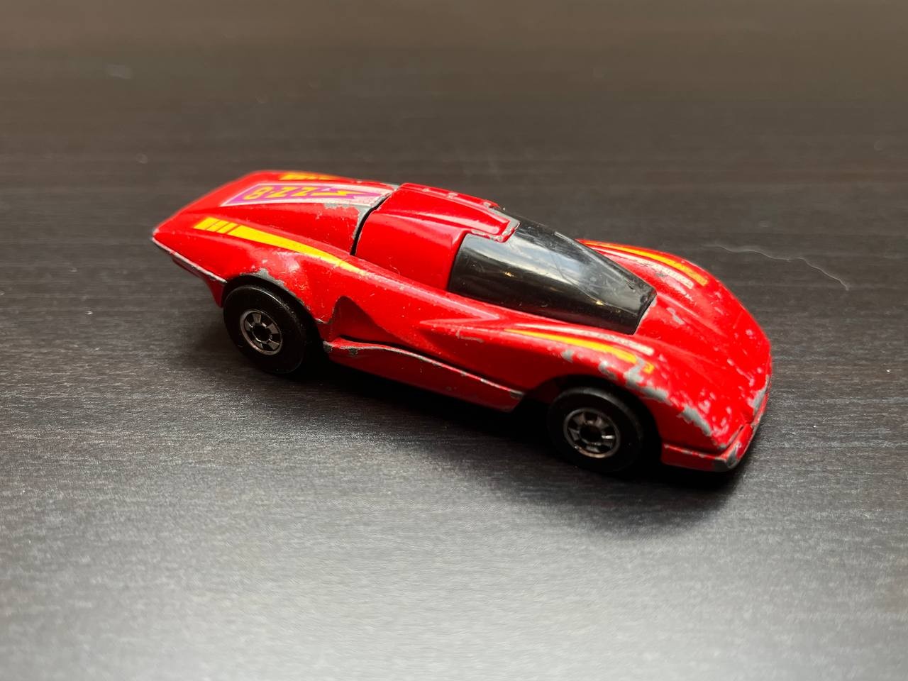 A red race car with a root that is hinged horizontally, so that when there is an impact, the roof flips over and then looks like it is damaged.